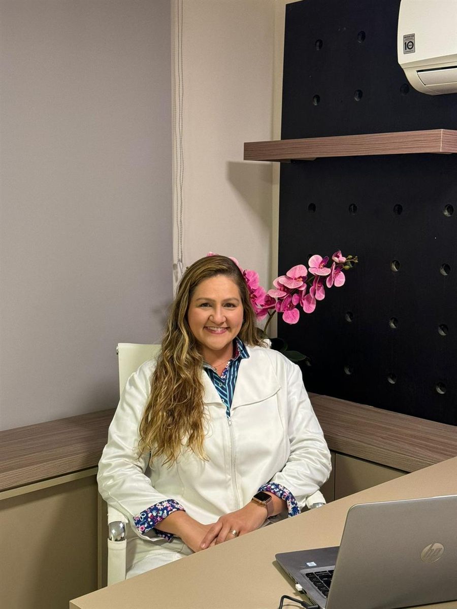 Dra. Raphaela Mannarino, cardiologista, de jaleco branco sentada no consultório