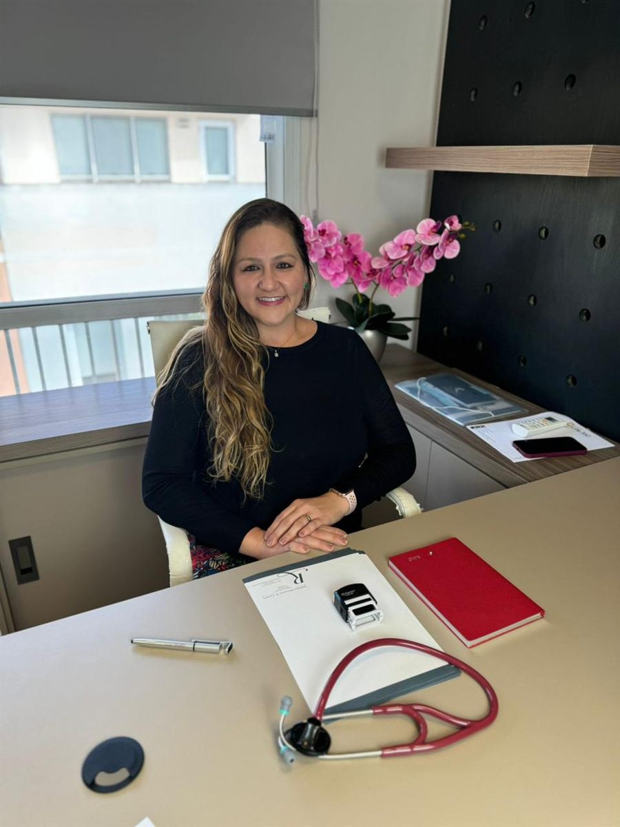Dra. Raphaela Mannarino à mesa do consultório, com o estetoscópio sobre a mesa