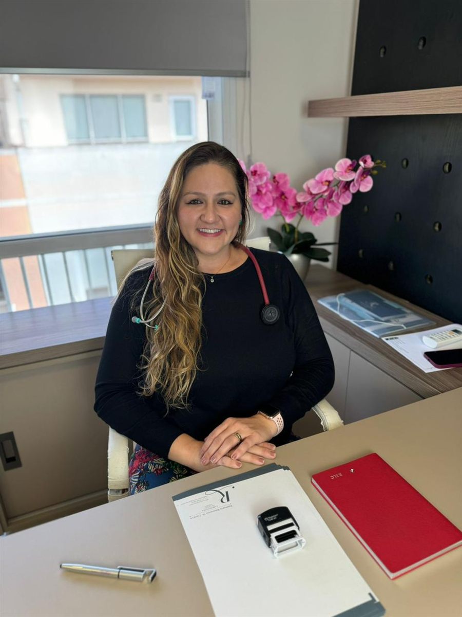 Dra. Raphaela Mannarino, cardiologista, sentada à mesa do consultório com o estetoscópio no pescoço